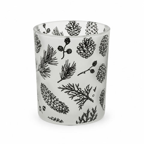 Ein windlichtglas mit schwarzen motiven aus pinienzapfen und immergrünen zweigen auf mattiertem glas