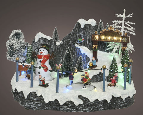 Led-winterszene dorftreiben mit festlicher miniatur-skisportanlage, schneemann, skifahrern und beleuchteten bergen