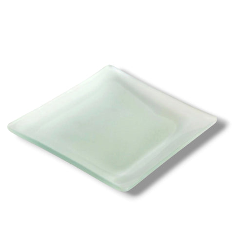 Ein mattes, eckiges kerzenteller aus glas in blassgrün mit weichen kanten und leichter glänzung