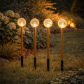 Vier glowing crackled glass globe lights mit goldenen stielen und schwarzen sockeln als Lumineo Gartenstecker set