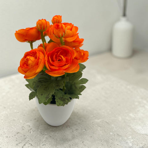 Eine lebhafte orange künstliche ranunkelblumen im eleganten weißen keramiktopf ranunkel orange