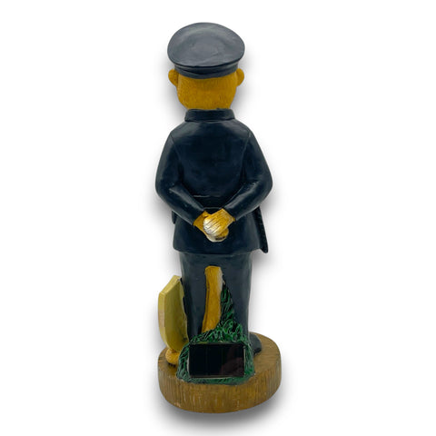 Solar-erdmännchen polizist figur 30cm in dunkelblauer uniform mit schwarzer mütze und goldenen handschuhen auf holzsockel neben grünem laub