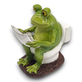 Grüne keramikfroschfigur sitzend auf weißer toilettenbrille mit silberner zeitung frosch auf wc 11x8x12 cm