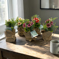 Vier blume im jutesäckchen mit rosa roten weißen und grünen kunstblumen in jute und mit schnur gebunden