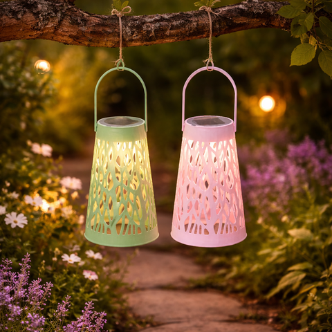 Zwei solar laternen warmweiß in pastellfarben grün und rosa mit filigranen mustern hängen an einem zweig