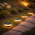 Runde solar bodenlampe 9x12cm mit schwarzem top und warm leuchtender weißer led basis entlang eines steinwegs