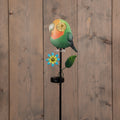 Grüner und orangefarbener solar-gartenstecker vogel mit leuchtendem auge und blauer blume auf schwarzem stab