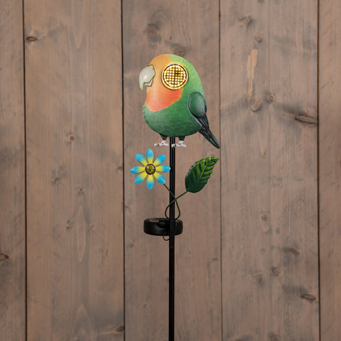 Grüner und orangefarbener solar-gartenstecker vogel mit leuchtendem auge und blauer blume auf schwarzem stab