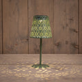 Grüne solar tischlampe aus metall mit filigranen blumenmustern und warmem licht auf holztisch