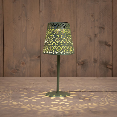 Grüne solar tischlampe aus metall mit filigranen blumenmustern und warmem licht auf holztisch