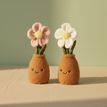 Zwei plüschblumen im topf mit lächelnden gesichtern und rosa sowie weißen flauschigen blüten