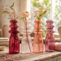 Set von vier vintage-glasvasen 7x20 cm in verlaufenden rosa tönen mit gestuften halsdesign und blumenarrangements