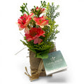 Ein charmantes künstliches blumenarrangement mit korallenfarbenen und pfirsichfarbenen blüten in jutesäckchen