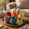 Set aus sechs bunten keramik kaffeebechern ohne griff mit rustikalen handgefertigten rändern und horizontalen rindungen