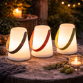 Drei beleuchtete led-laternen outdoor mit zylinderförmigem design und bunten lederriemen in schwarz rot und grün auf holz