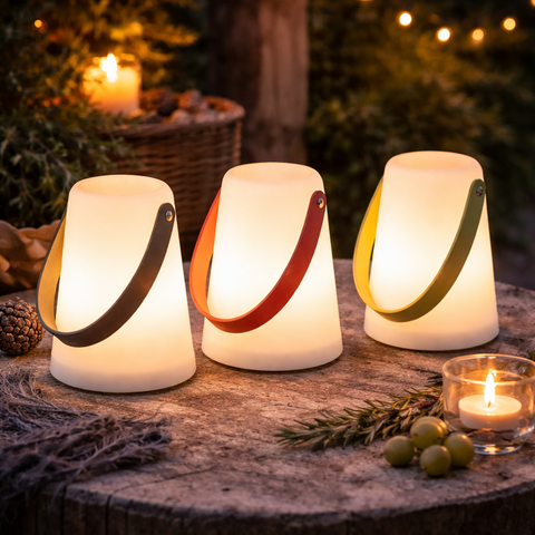 Drei beleuchtete led-laternen outdoor mit zylinderförmigem design und bunten lederriemen in schwarz rot und grün auf holz