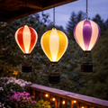 Drei beleuchtete led solar heißluftballonlichter mit flackereffekt in rot weiß gelb weiß und lila weiß mit schwarzen metallkörben