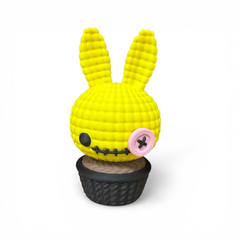3d voodoo-hase eine hellgelbe gehäkelte hasenfigur mit rosa knopfähnlichem auge in einem schwarzen cupcakeschälchen