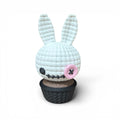 3d voodoo-hase weiße gehäkelte hasenfigur mit rosa knopfnase sitzt auf schwarzer texturierter cupcake-basis