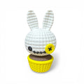 Weißer gehäkelter 3d voodoo-hase mit gelbem knopfauge und gesticktem gesicht in gelbem cupcake-halter sitzt