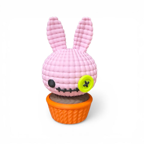 Rosa gehäkelte 3d voodoo-hase aus garn mit gesticktem gesicht und limonengrünem knopfauge in orange gestricktem cupcake-sitz