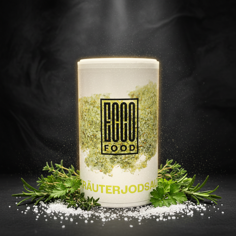 Weißer zylinderförmiger behälter von eco food kräuter jodsalz mit grünen getrockneten kräutern sichtbar im und um den behälter