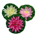 Drei künstliche lotusblumen aus polyester in pink weiß und magenta auf glänzenden grünen blättern