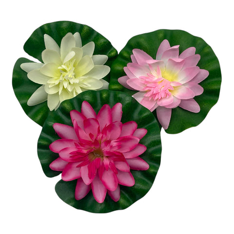 Drei künstliche lotusblumen aus polyester in pink weiß und magenta auf glänzenden grünen blättern