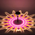Eine schwarze solar-gartenlampe mit rundem facettiertem kopf wirft ein pink-gelbes 360° muster auf den boden