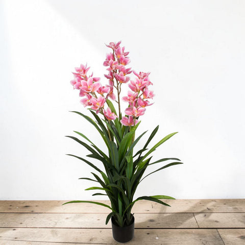 Eine hohe künstliche rosa orchidee mit üppigen grünen blättern und zarten blüten in einem schwarzen topf