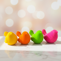 Vier bunte vogel radiergummis in gelb orange grün und rosa aus weichem material auf marmoroberfläche angeordnet