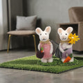 Zwei dekorative filzmaus figurinen aus weißer wolle, eine mit rosa kleid und karotte, die andere mit lila overall und blumenstrauß
