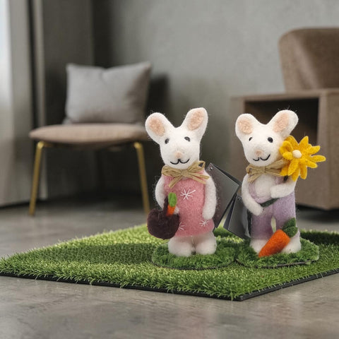 Zwei dekorative filzmaus figurinen aus weißer wolle, eine mit rosa kleid und karotte, die andere mit lila overall und blumenstrauß
