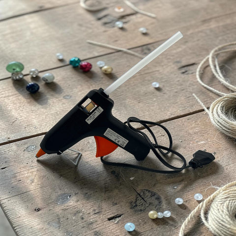 Schwarze und orange Heißklebepistole 40 Watt mit weißer Düse auf Holzoberfläche liegend