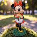 Gartenfigur minnie in rot mit schleife aus glänzendem kunststoff hält bunten blumenstrauß mit schwarzen ohren und gelben schuhen