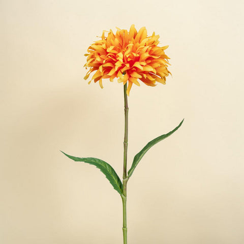 Ein lebhaft orange-gelber künstlicher spider gerbera mit mehrlagigen blütenblättern und glänzenden grünen blättern