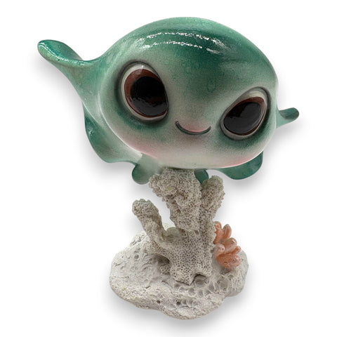 Cute teal-farbene harzfigur eines babywals mit großen schwarzen augen und rosa wangen auf texturierter korallenbasis rochen gloss grün