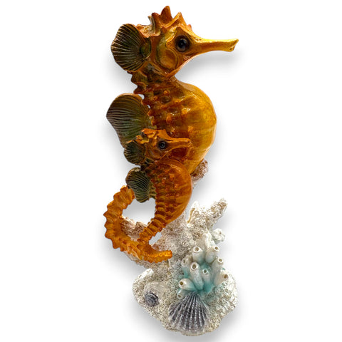 Golden-orange seepferdchen figurine mit grün getönten flossen und glänzender struktur auf korallen und muschel basis