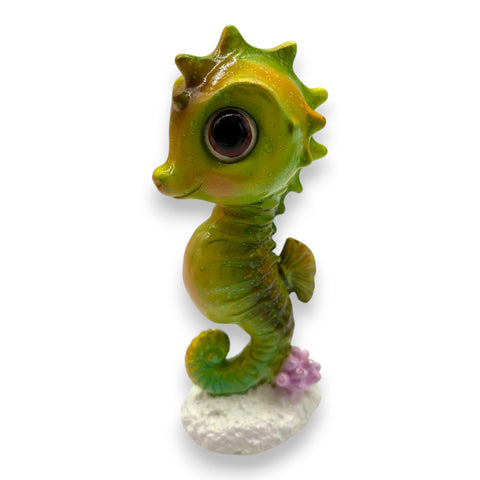 A charmantes seepferdchen gloss grün orange figurine mit großen augen steht auf weißer basis mit lila korallen
