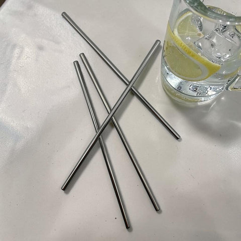 Vier elegante metallene edelstahl-trinkhalme in silber liegen gekreuzt auf weißem untergrund